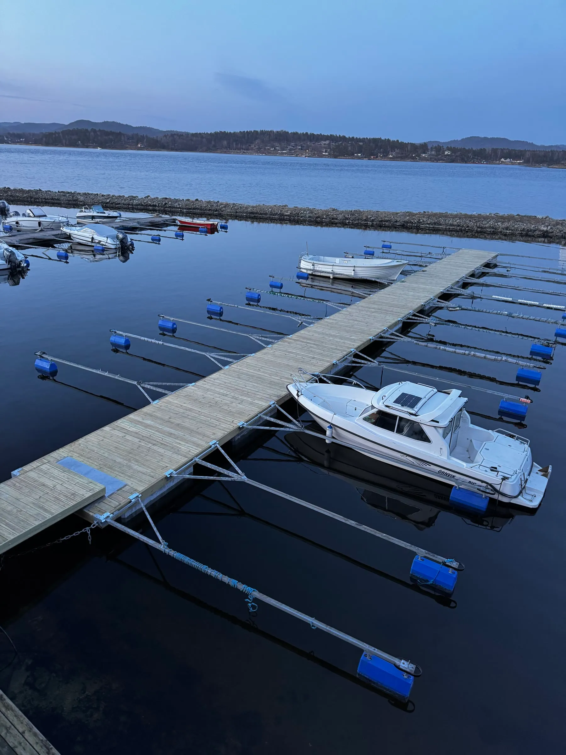Ferdig bryggeanlegg med trebrygge, utriggere og båter i en lun havn.